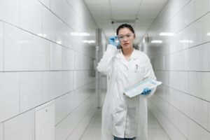 Une scientifique asiatique marchant dans un couloir de laboratoire avec des lunettes de protection et une blouse de laboratoire.